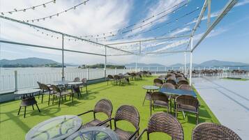 An outdoor seating area with tables and chairs, a view of the sea, and a white fence.