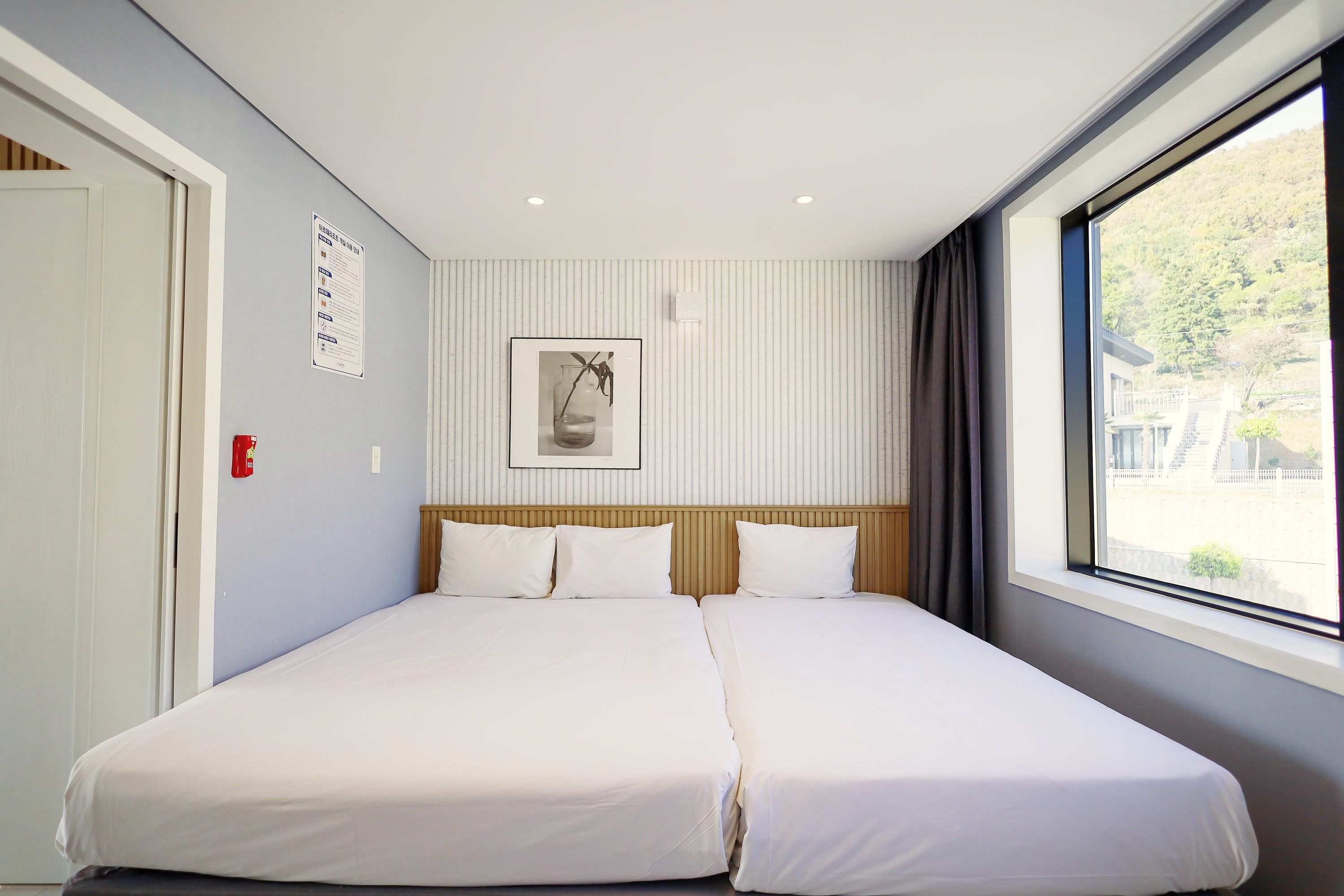 Een tweepersoonsbed in een hotelkamer, met uitzicht op een gebouw en bomen buiten het raam.
