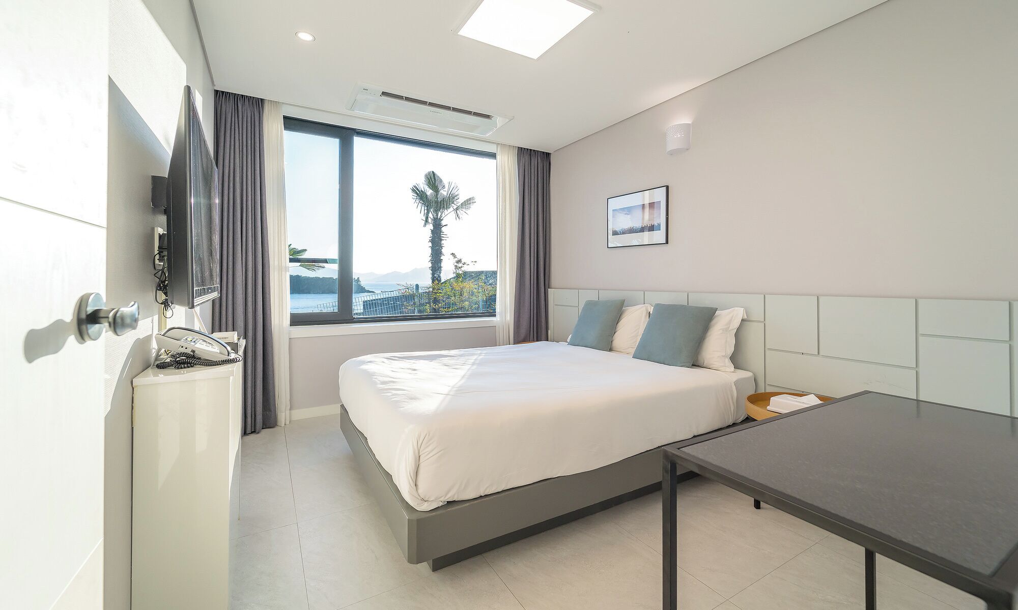 Una habitación de hotel moderna con una cama, una mesita de noche y un ventanal con vista al mar.