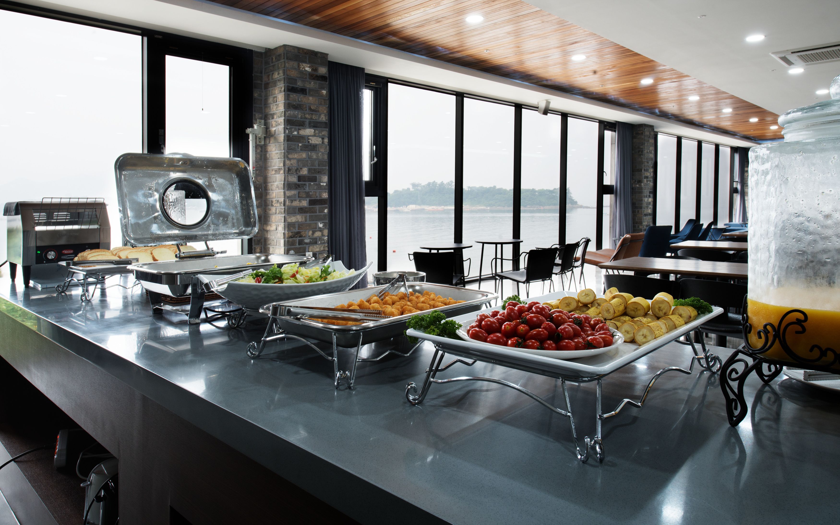 Ein Buffet mit verschiedenen Speisen und einer Grillstation, gelegen in einem Raum mit großen Fenstern und Meerblick.