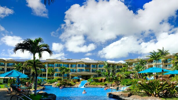 Ein Resort mit großem Pool, Palmen und einem mehrstöckigen Gebäude mit Balkonen.
