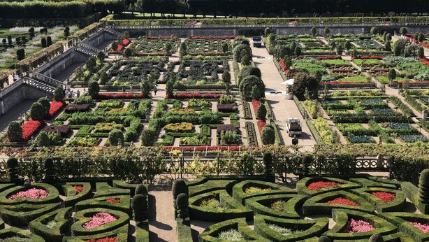 An aerial view of a meticulously landscaped garden with geometric pathways and symmetrical flower beds.