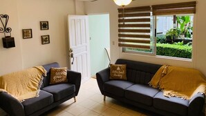 Ein Wohnzimmer mit zwei dunklen Sofas, einem Deckenventilator und einem Fenster mit Jalousien.
