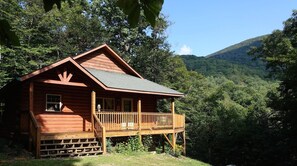 Een houten chalet met een veranda, omgeven door weelderige begroeiing en bergen.
