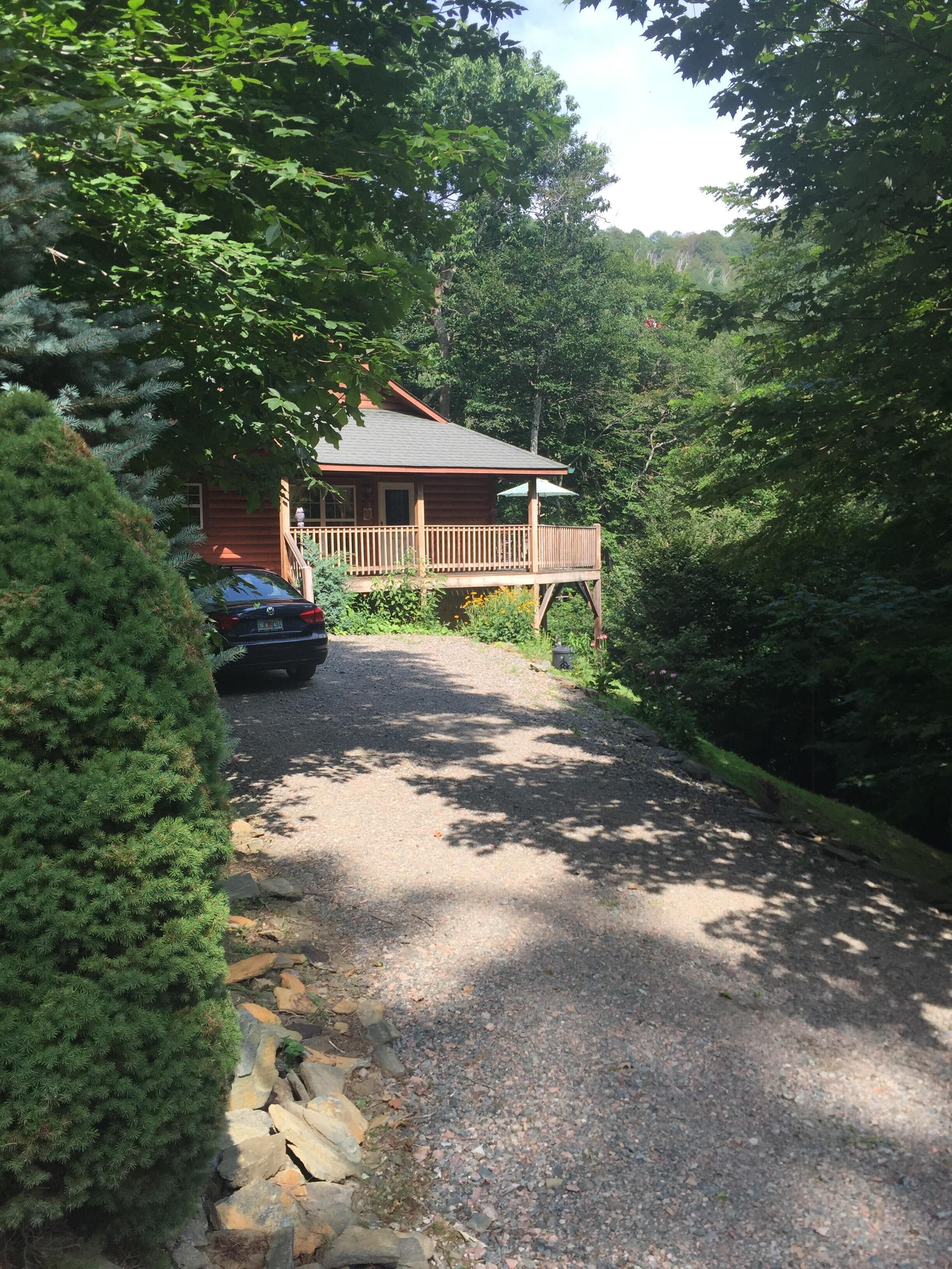 A cabin with a wooden deck and a gravel driveway leading to it.