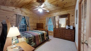 Een slaapkamer in een houten chalet, met een bed, een dressoir, een spiegel en een plafondventilator.