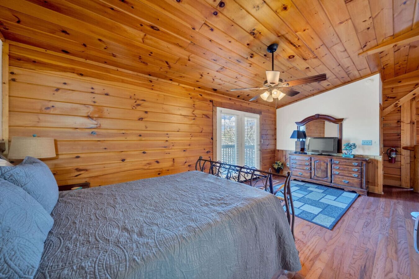A wooden cabin bedroom with a bed, a desk, and a television.