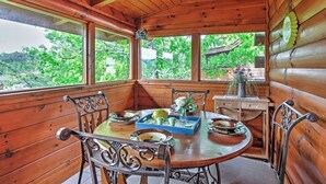 Interior de una cabaña de madera con una mesa de comedor, sillas y una ventana con vistas a la vegetación.