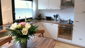 A modern kitchen with white cabinets, a stainless steel stove, and a window with blinds. - Spacious apartment right on the Fürstenauer castle (Fürstenau)