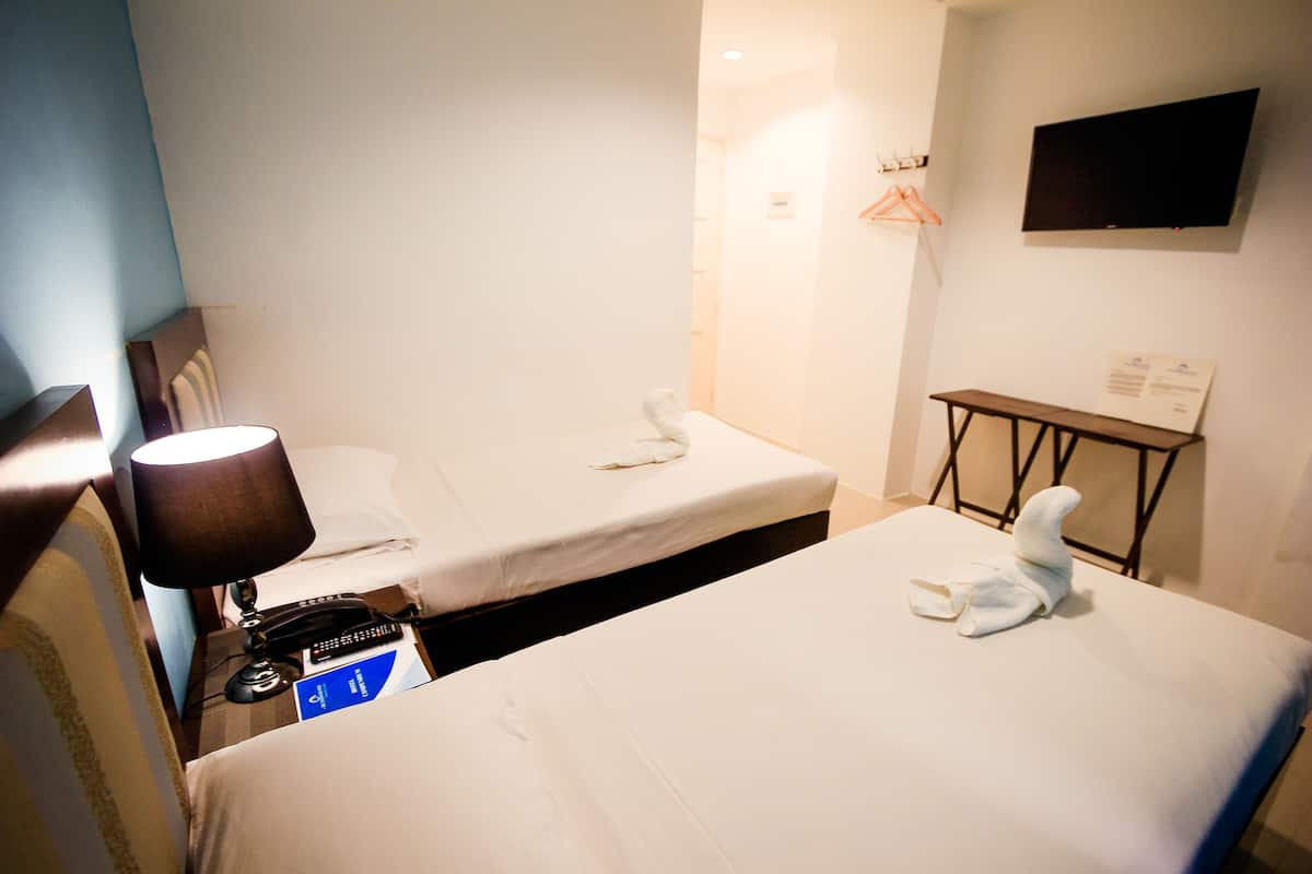 Une chambre d’hôtel avec deux lits, une table de chevet avec une lampe, un téléviseur fixé au mur et une petite table avec une serviette.