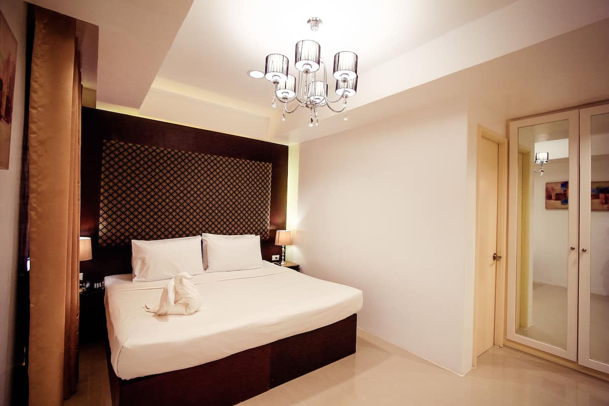 Une chambre d’hôtel avec un grand lit, un lustre, une tête de lit à motifs et une armoire.