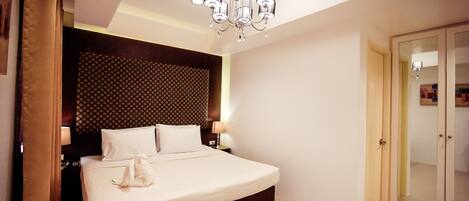 A hotel room with a large bed, a chandelier, a patterned headboard, and a wardrobe.