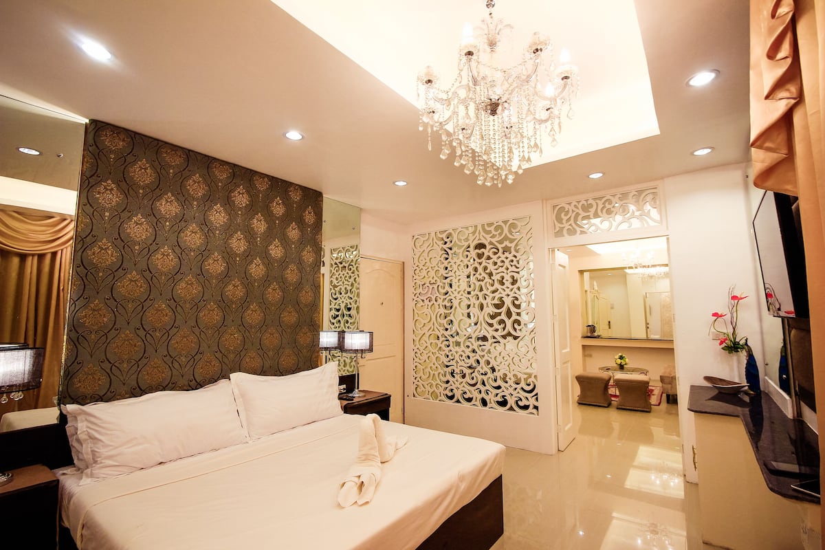 Une chambre d’hôtel bien éclairée, dotée d’un grand lit, d’un lustre et d’un panneau décoratif mural.