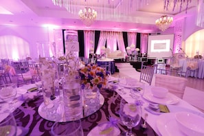 A banquet hall with round tables set for a formal event, featuring floral centerpieces and elegant table settings.