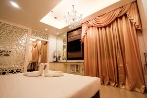 A hotel room with a bed, a chandelier, a TV, and curtains.