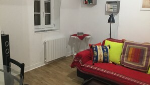En hyggelig stue med en rød sofa, et lille hvidt bord, en bogreol og en radiator.