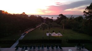 Une vue sur le coucher de soleil depuis une terrasse équipée de chaises longues et d’une plateforme qui s’étend au-dessus d’une zone herbeuse.