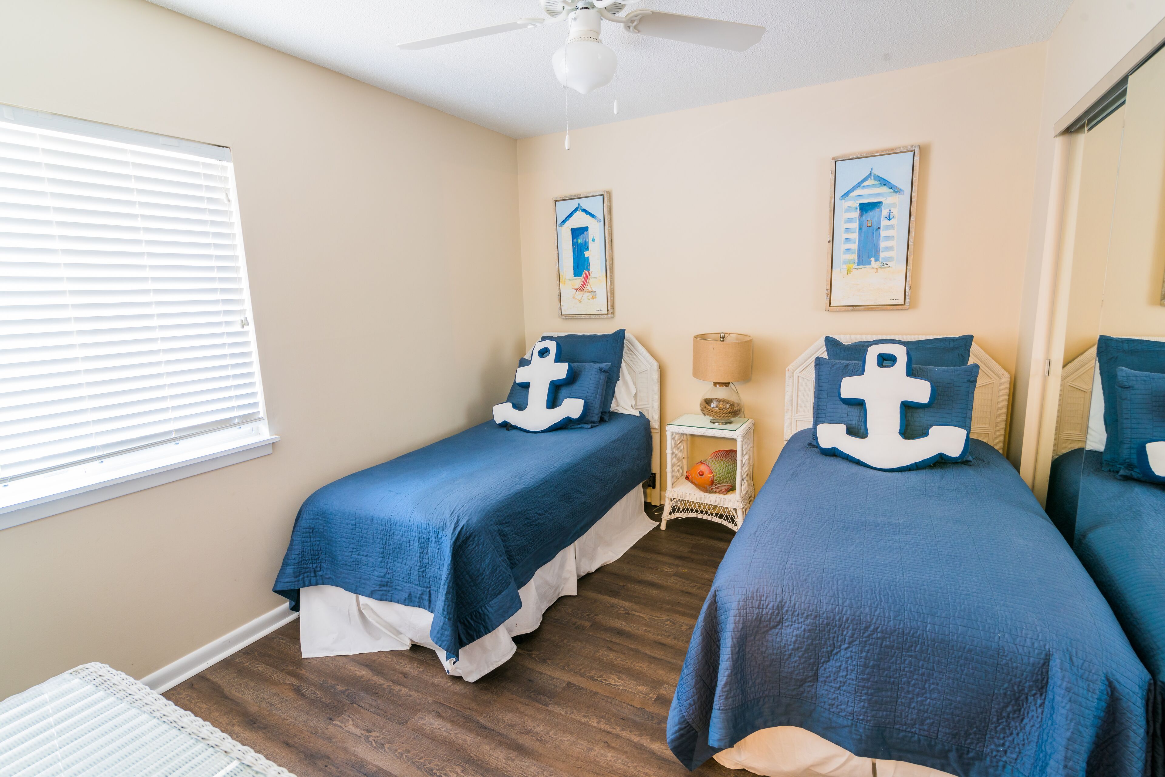A bedroom with two beds, a ceiling fan, and two nautical-themed wall art pieces.