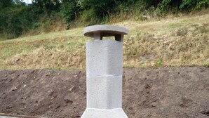 Ein aus Beton gefertigter Pizzaofen im Freien mit Schornstein, integriert in eine Ecke einer Holzterrasse.