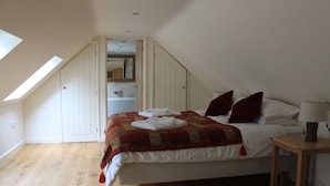 Ein Schlafzimmer mit schrägen Wänden, einem Bett mit rotem und weißem Quilzdecke, einem Nachttisch aus Holz und einem Spiegel über dem Bett.
