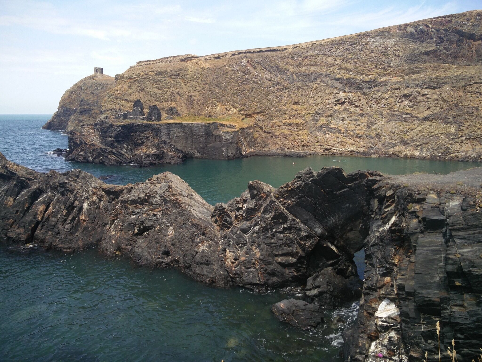 A coastal landscape with rocky terrain and a small structure on a hill.