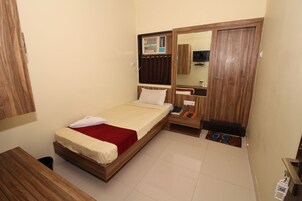 Un dormitorio con cama, un escritorio de madera, armario, espejo y una mesita con pantuflas.