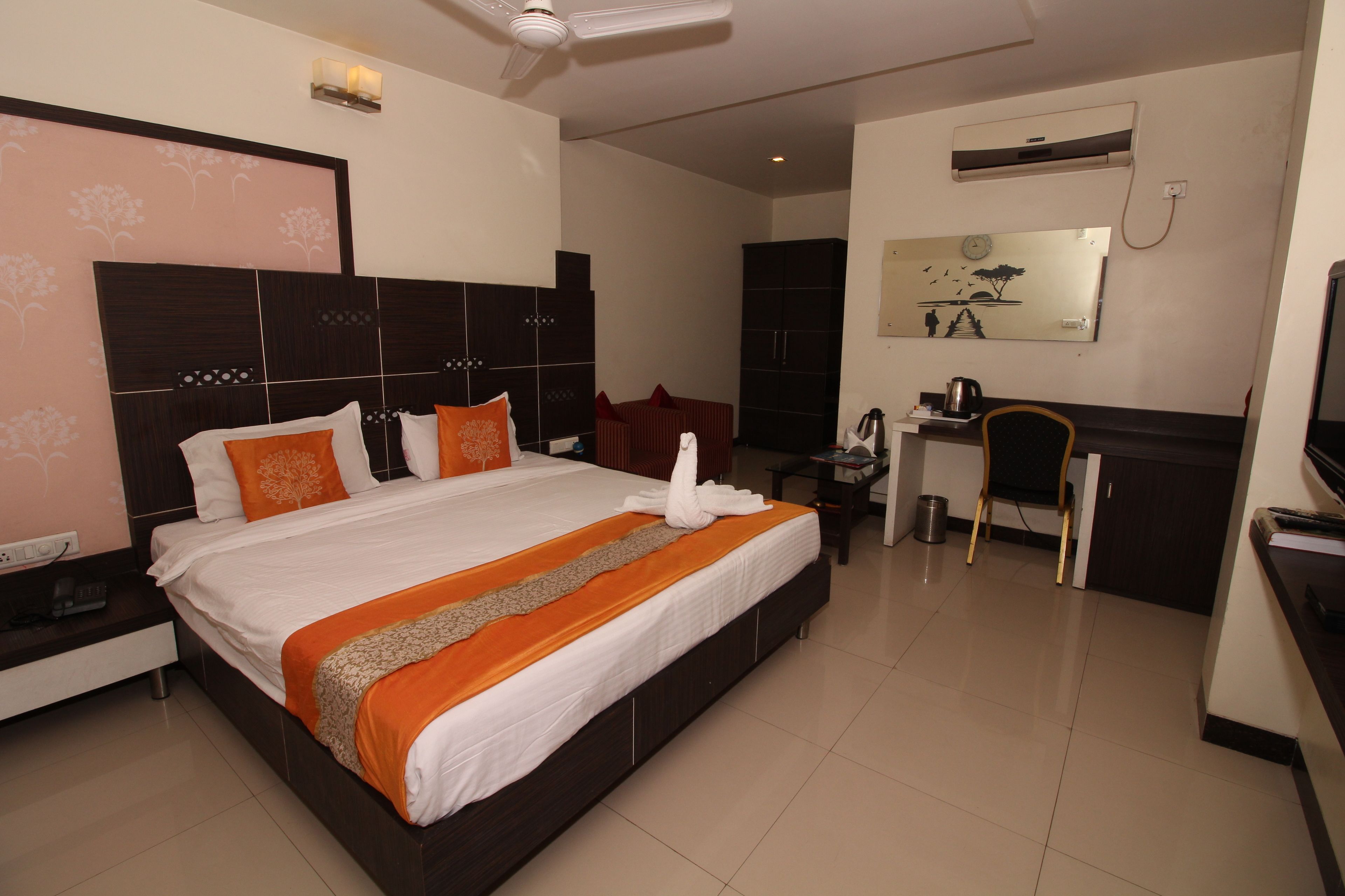 Quarto de hotel com uma cama grande, uma escrivaninha, uma cadeira, um espelho e um ar condicionado.