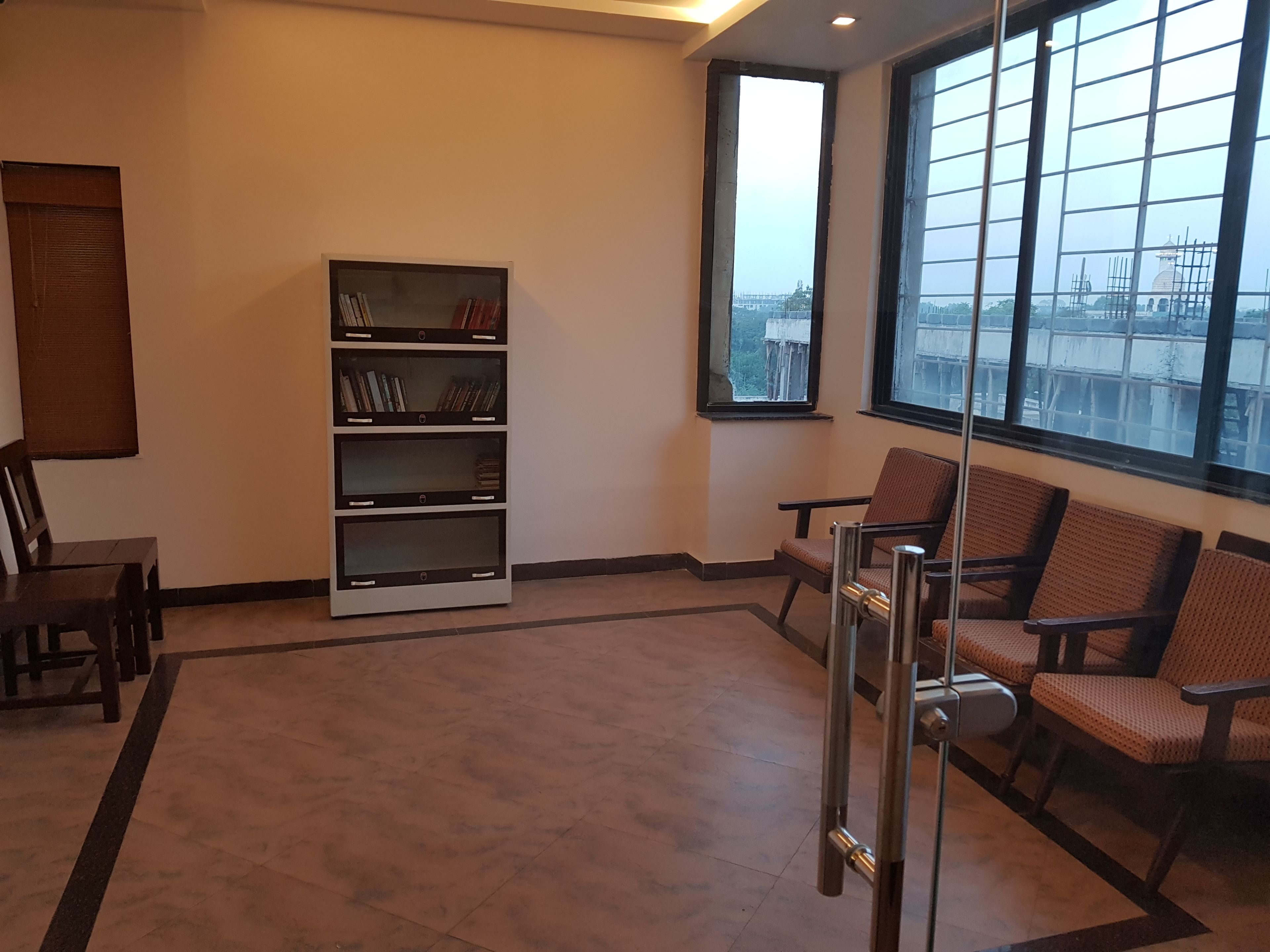 A waiting area with a bookshelf, chairs, and a large window with a view of a bridge.
