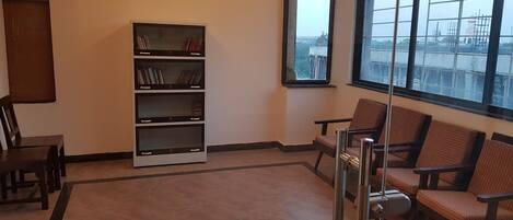 A waiting area with a bookshelf, chairs, and a large window with a view of a bridge.
