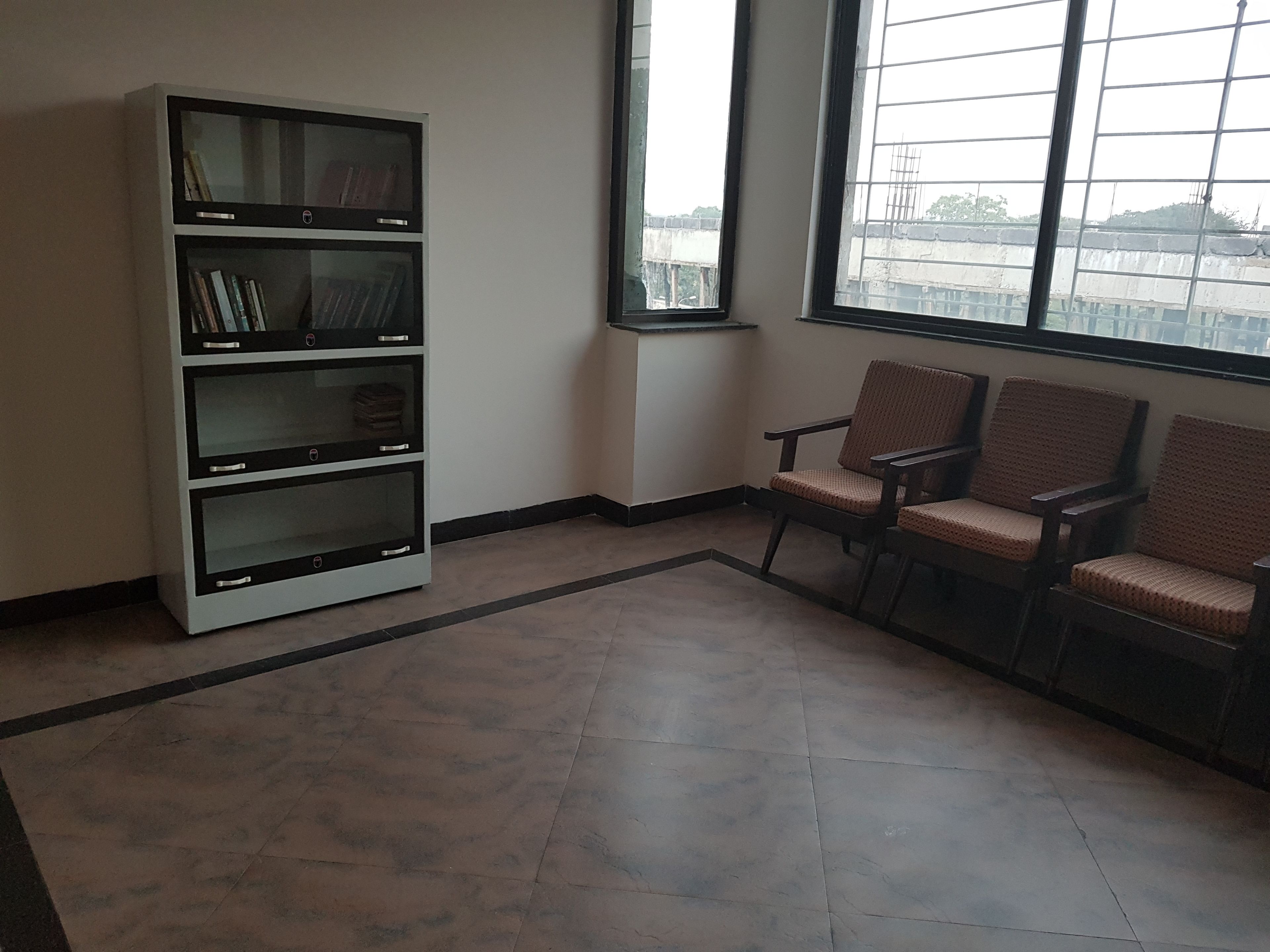 A room with a large bookshelf, three wicker chairs, and a large window with a view of a bridge.