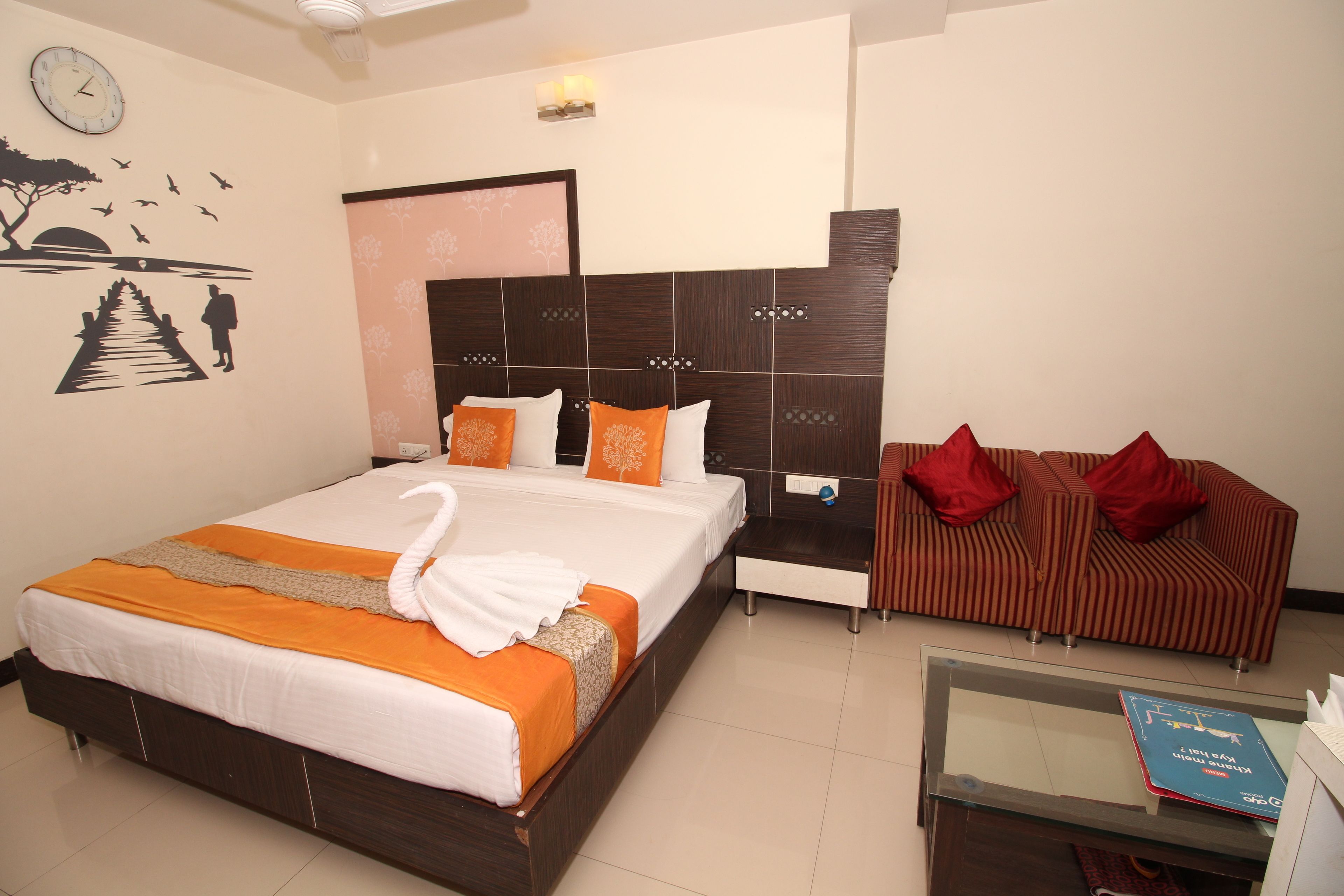 Een hotelkamer met een groot bed, een bank, een glazen bijzettafeltje en een wandklok.