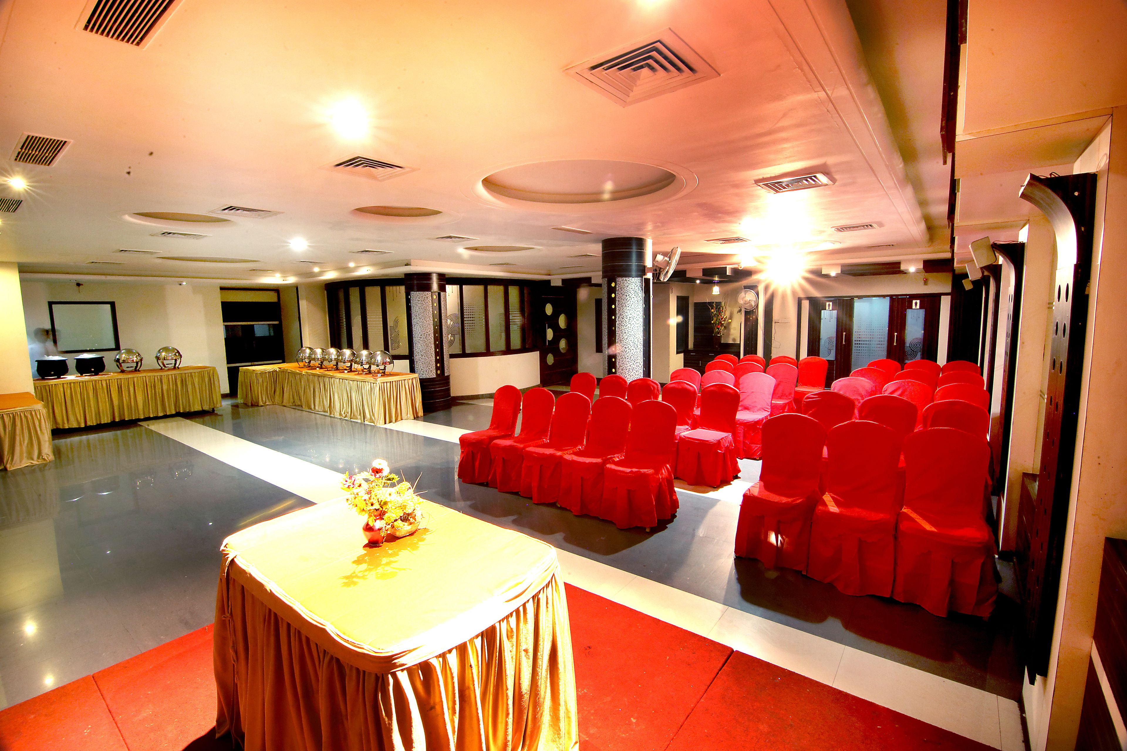 Un salón de conferencias con un escenario, hileras de sillas rojas y una mesa cubierta con un mantel amarillo.