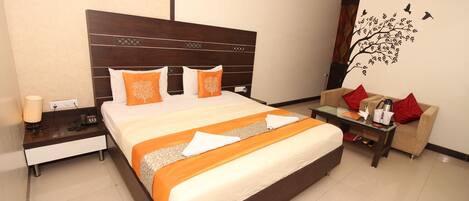 A hotel room with a large bed, a nightstand, a coffee table, and a sofa.