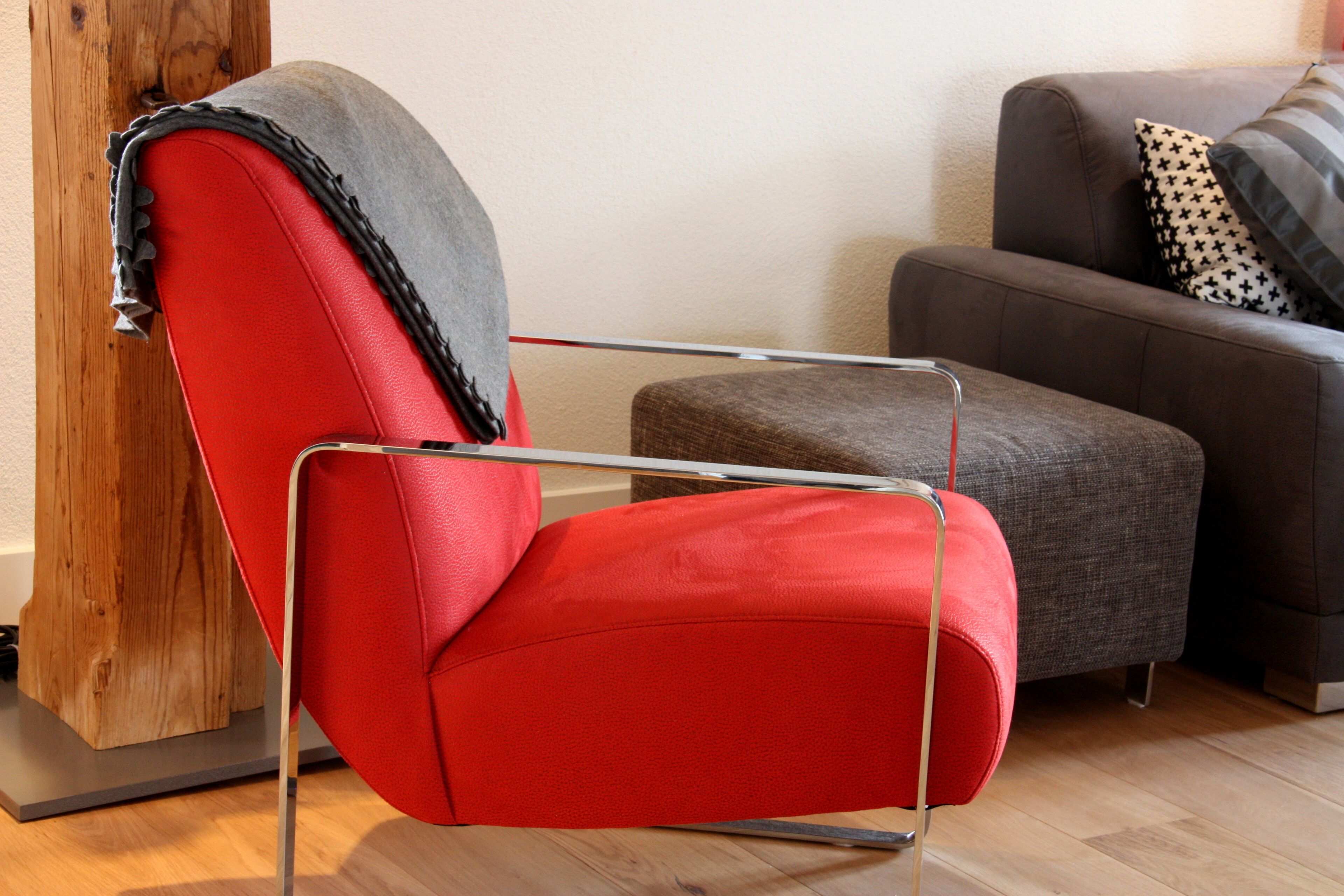 Un salon moderne avec un fauteuil rouge, un canapé gris et un élément décoratif en bois.
