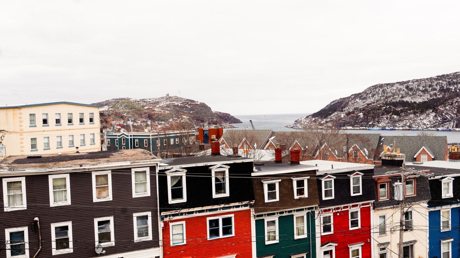A row of colorful buildings with a view of a snowy landscape and a body of water in the distance.