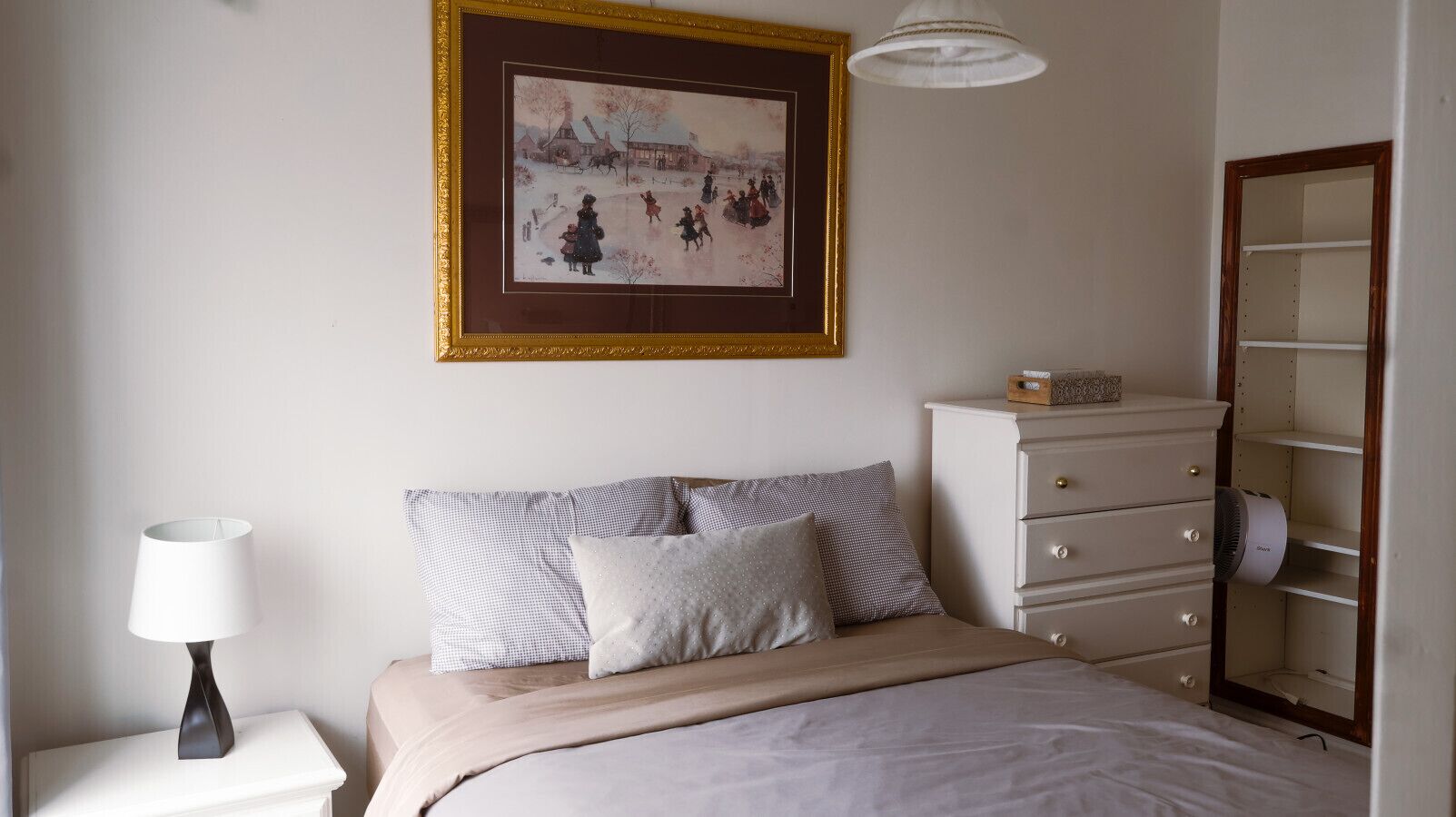Une chambre à coucher comprenant un lit, une commode, une lampe, un tableau encadré au mur et une armoire.