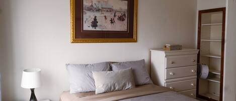 Une chambre à coucher comprenant un lit, une commode, une lampe, un tableau encadré au mur et une armoire.