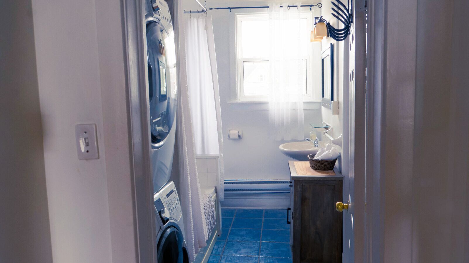 Un baño con piso de azulejos azules, un lavamanos blanco, un espejo y una cortina de ducha.