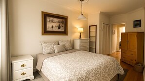 Un dormitorio con cama, mesitas de noche, armario, lámpara y un cuadro en la pared.