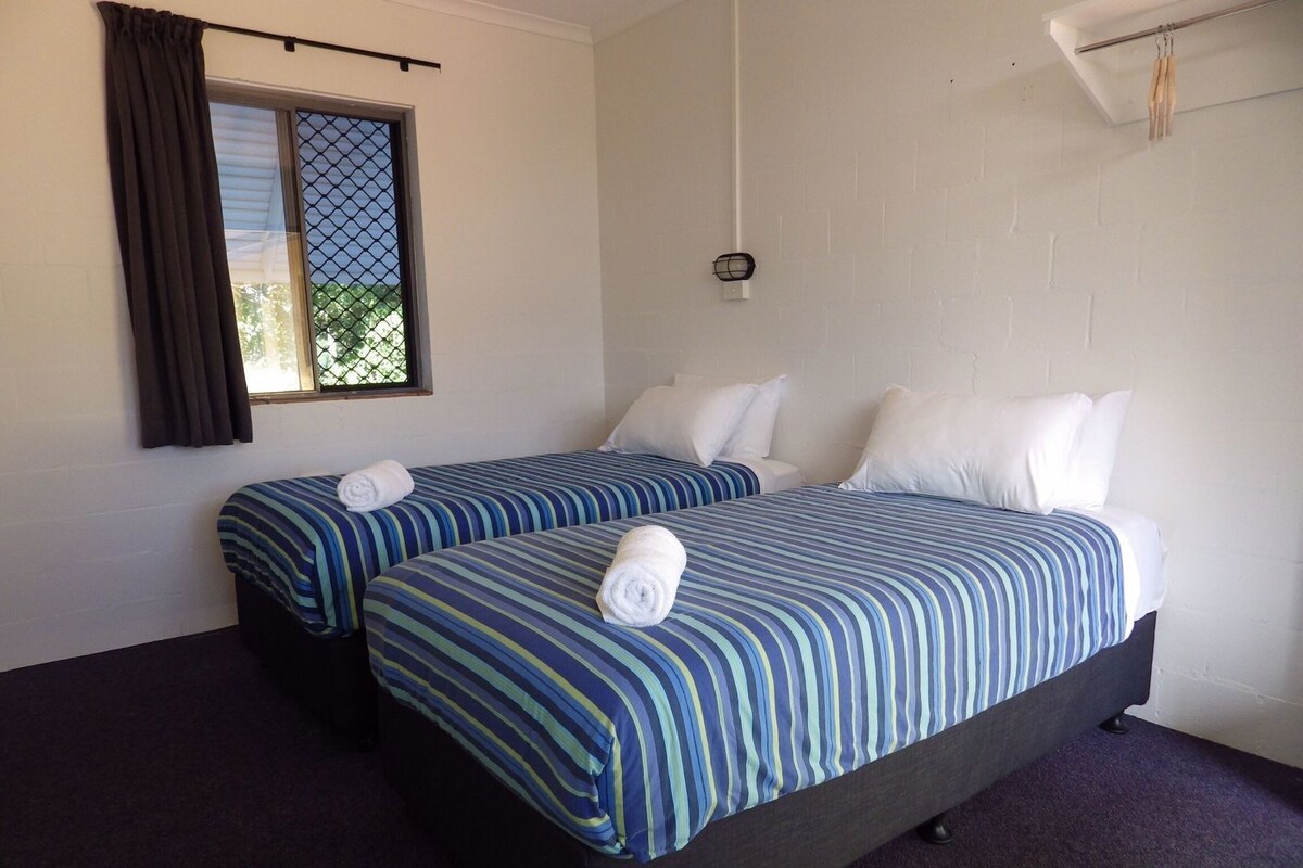 A room with two beds, each with striped bedding and white pillows, a window with curtains, and a hanging light fixture.