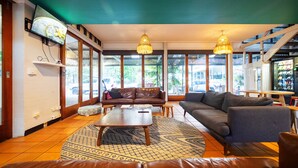 A spacious lounge area with leather sofas, a coffee table, and patterned rugs. Large windows allow natural light and views of the outside. - YHA Cape Byron (Byron Bay)