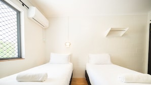 A room with two single beds, a window with a mesh screen, an air conditioning unit, and a light fixture. - YHA Cape Byron (Byron Bay)