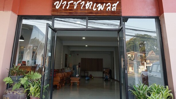 A hotel entrance with a sign above the door, potted plants, and a visible interior with furniture. - Parichart Place (Pua)