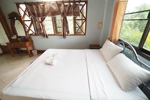 A neatly made bed with white linens and pillows, a wooden dresser with a mirror, and a window with curtains.