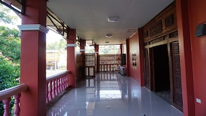 A corridor with red walls, a tiled floor, and a wooden gate leading to an outdoor area. - Parichart Place (Pua)
