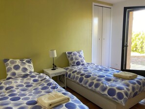 A room with two beds, each with a blue and white polka dot bedspread and matching pillows. There is a white nightstand with a lamp and a small drawer labeled "NEWPORT". A door leads to an outdoor area. - Family property with large swimming pool, park and superb landscape as far as the eye can see (Tourtour)
