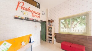 A reception area with a sign for 'Pachumas Hotel', a reception desk, a red sofa, a bookshelf, and a window with blinds. - Pachumas Mansion (Karon)