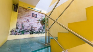 A staircase with yellow walls and a stone wall with a framed picture and plants. - Pachumas Mansion (Karon)