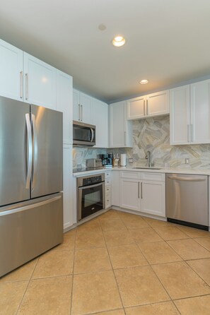 Enjoy cooking in this well-equipped kitchen with a refrigerator, microwave, and dishwasher, set against a backdrop of white cabinetry and large tile flooring.