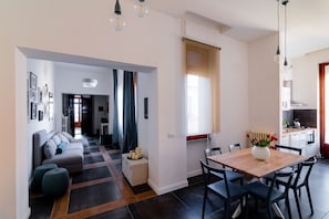 Una sala de estar moderna con un sofá, otomanas y una mesa de comedor con sillas. Hay una zona de cocina con estufa y armarios.